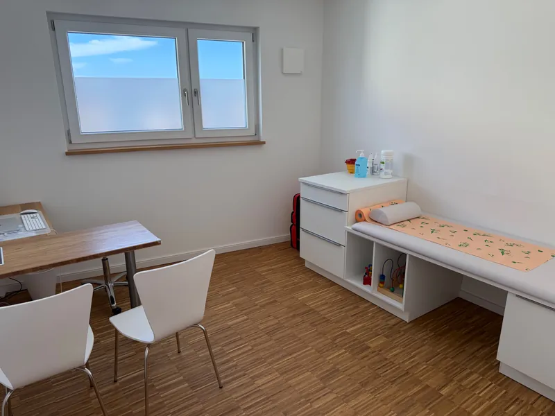 Behandlungszimmer mit Schreibtisch, Stühlen und Untersuchungsliege