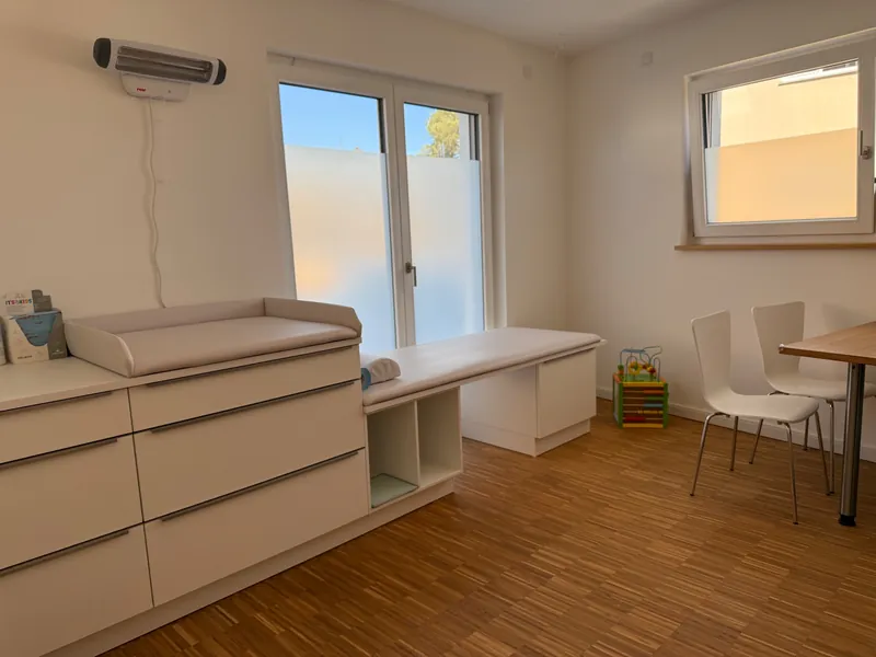 Behandlungszimmer mit Wickeltisch, Wärmestrahler, Untersuchungsliege und Sitzplätzen