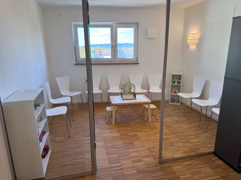 Helles Wartezimmer mit weißen Stühlen, Kindertisch, Spielzeug und Bücherregal
